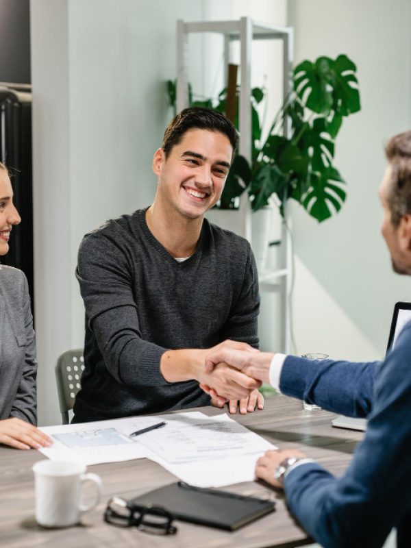 young-happy-couple-making-agreement-with-their-financial-advisor-home-men-are-shaking-hands
